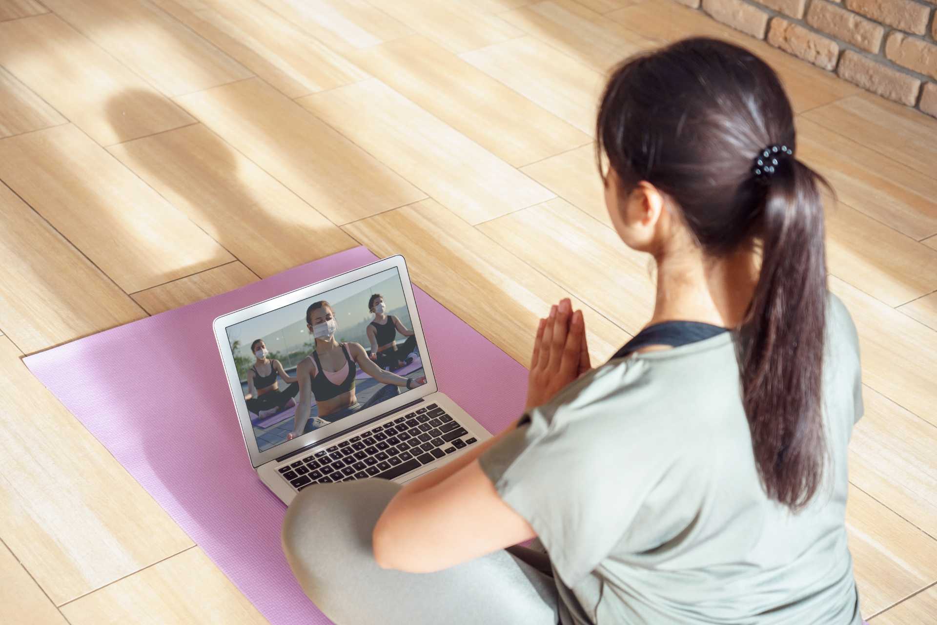 Frau praktiziert Yoga vor Laptop